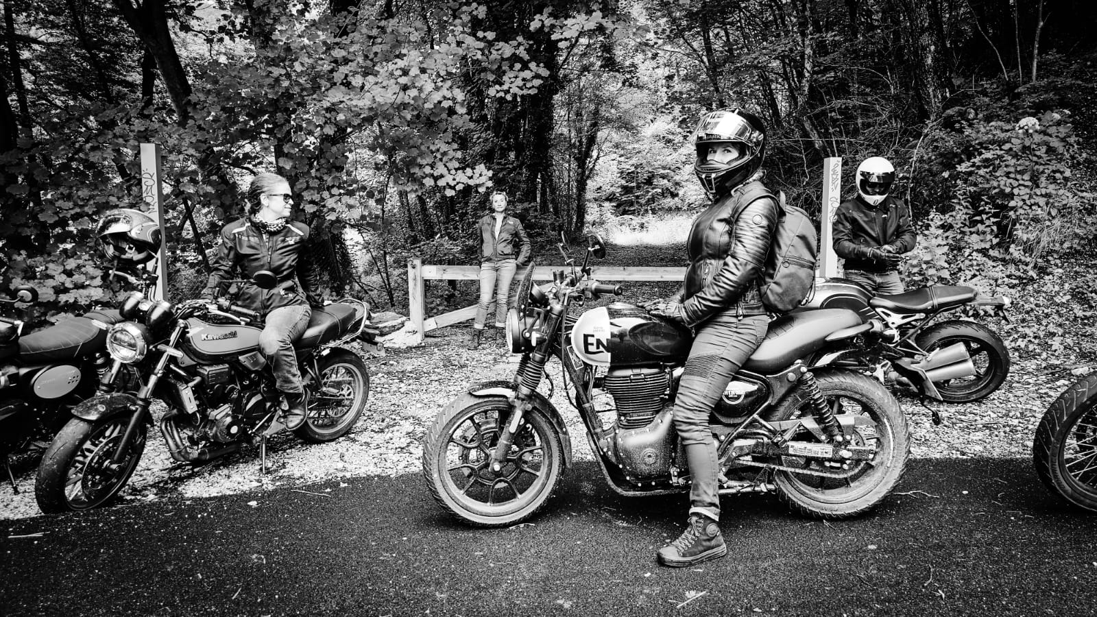 Photo en noir et banc, en bord de route dans la montée d'un col, dans le Vercors. Au premier plan, Nathalie sur sa Royal Enfield, au second plan à gauche, Magali sur une Z650 RS Kawasaki de l'agence de voyages à moto et au troisième plan, Jocelyne en passagère. A l'arrière plan, un chemin qui mène dans la forêt