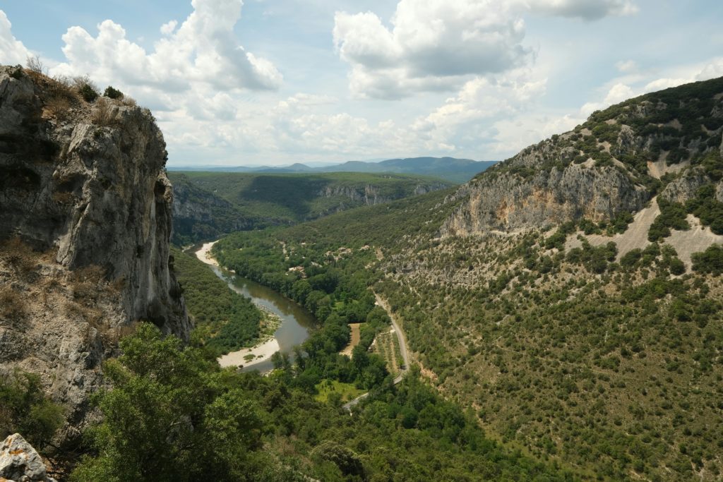 Au milieu de l'image, les gorges de l'Ardèche et la route qui la surplombe sinuent jusqu'à l'arrière plan. Deux rocs montagneux encadrent les routes fluviale et bitumeuse, tandis qu'à l'arrière plan, les monts du sud de l'Ardèche se dessinent