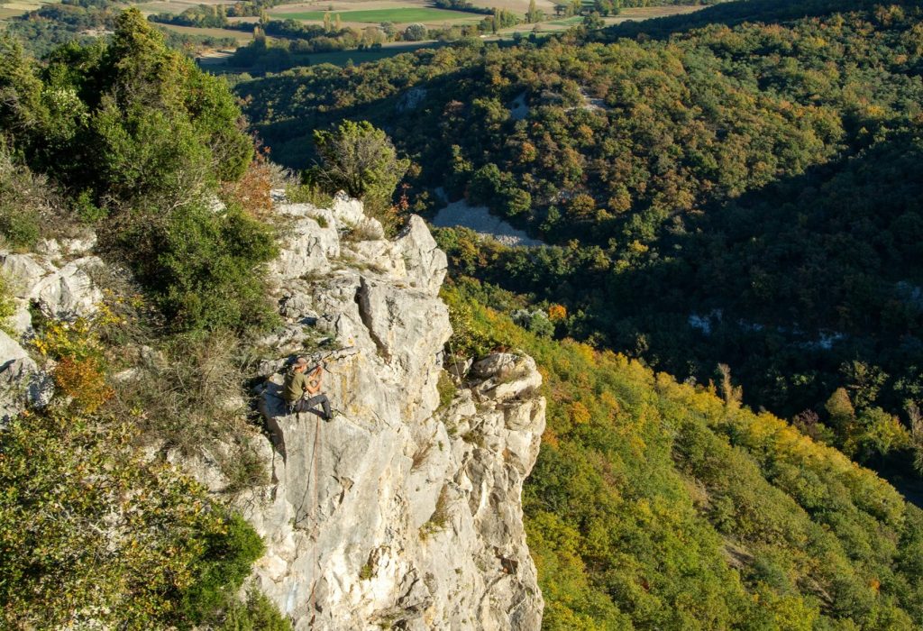 L'image représente les monts d'Ardèche, avec au premier plan un aplomb rocheux propice à l'escalade, en contre-bas une forêt et à l'arrière plan collines, forêts et monts typiquement ardéchois